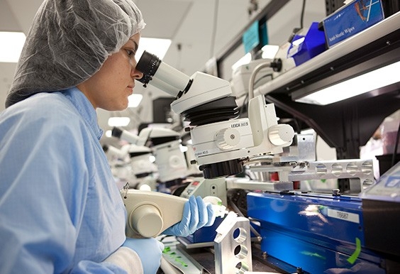 Professional wearing cleansuit, looking through a microscope