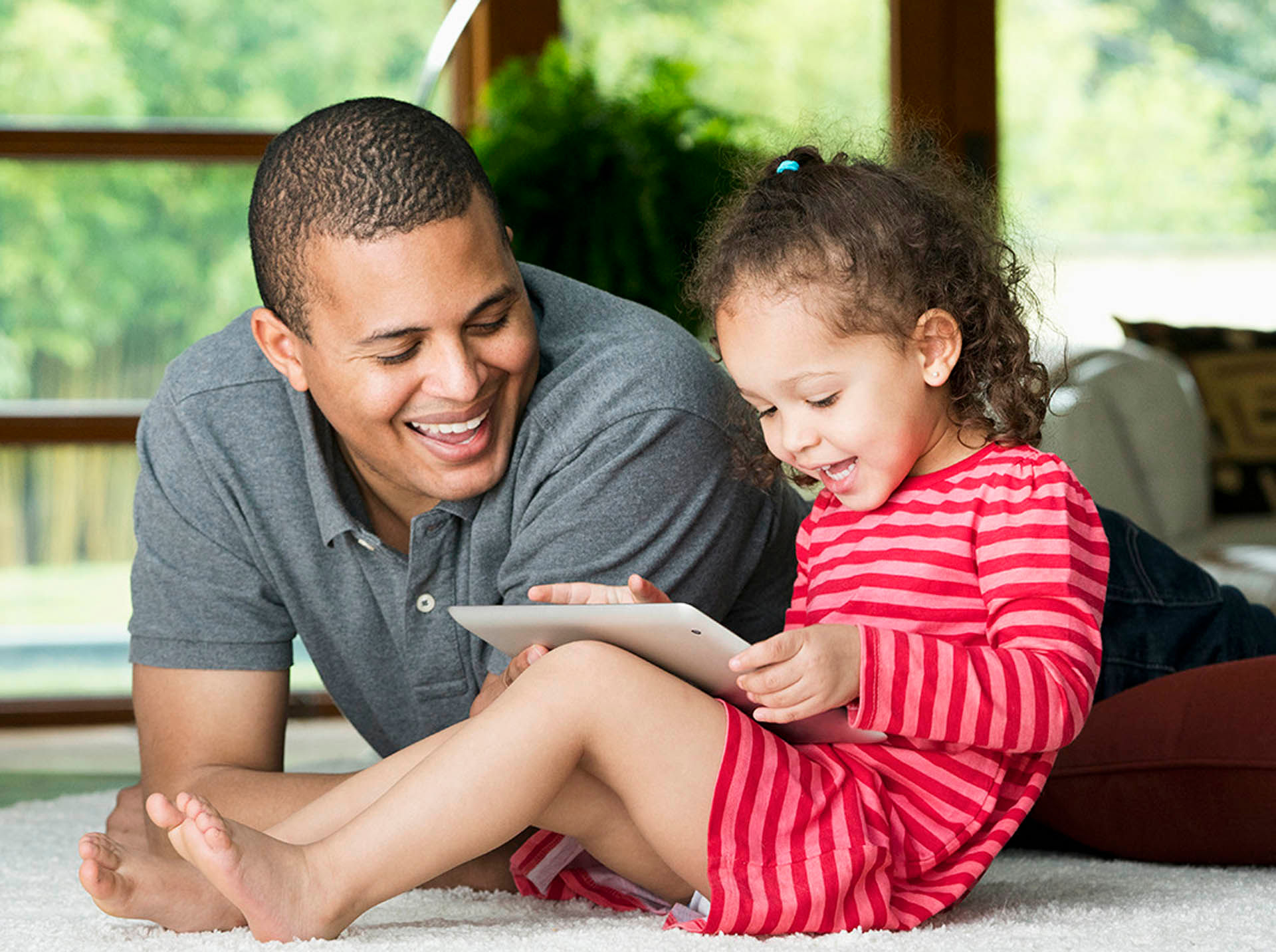 Father watching daughter using digital tablet on floor