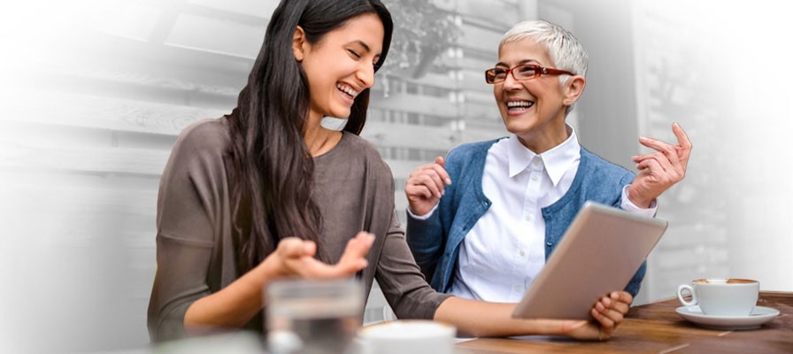 a mature woman and a younger woman looking at a tablet and laughing