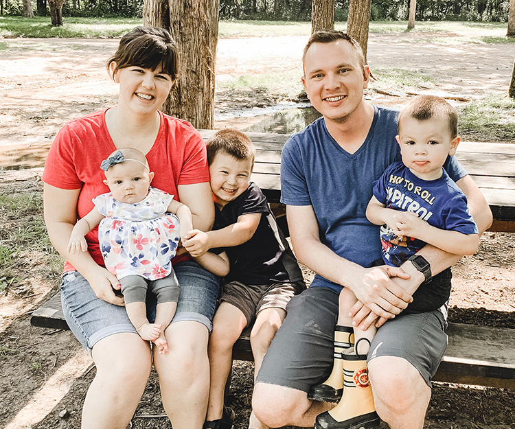 A father with a cochlear implant sits on a bench with his wife and two children