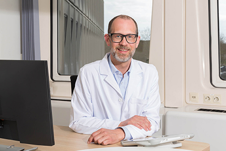 A professor in a lab coat poses for a picture.